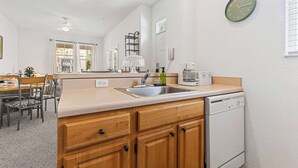 Una cocina compacta con lavavajillas, un lavaplatos, un reloj y una zona de comedor con sillas y una mesa.