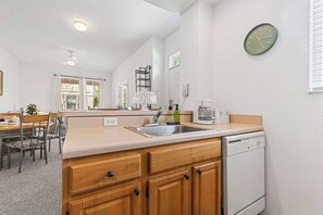 Una cocina compacta con lavavajillas, un lavaplatos, un reloj y una zona de comedor con sillas y una mesa.