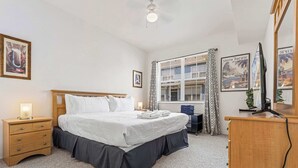 Un dormitorio con cama, mesitas de noche, un escritorio, una silla, un televisor y cuadros en las paredes.