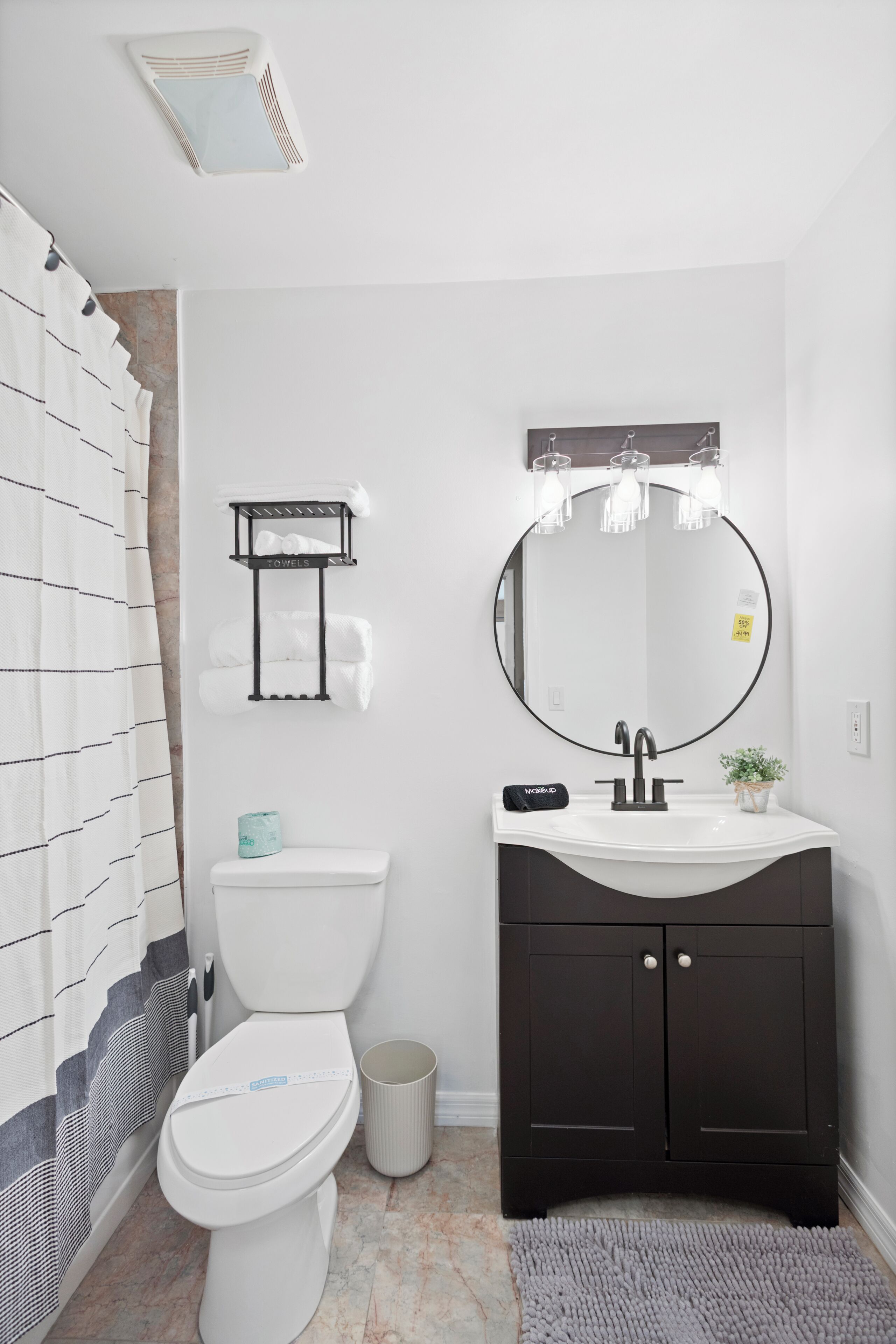 Un baño con inodoro blanco, tocador negro con espejo y perchero.