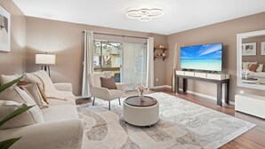 Una sala de estar moderna con sofá, sillón, mesa de centro, televisor y un gran ventanal con cortinas.