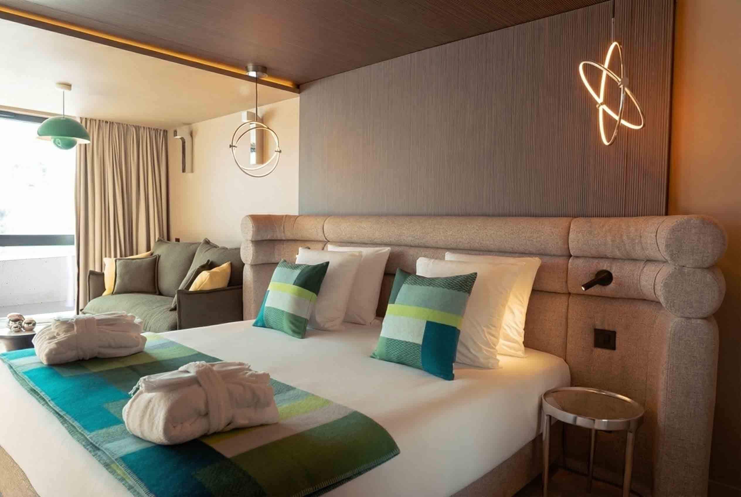 Une chambre d’hôtel avec un grand lit, un applique ronde au mur et une vue sur l’extérieur.