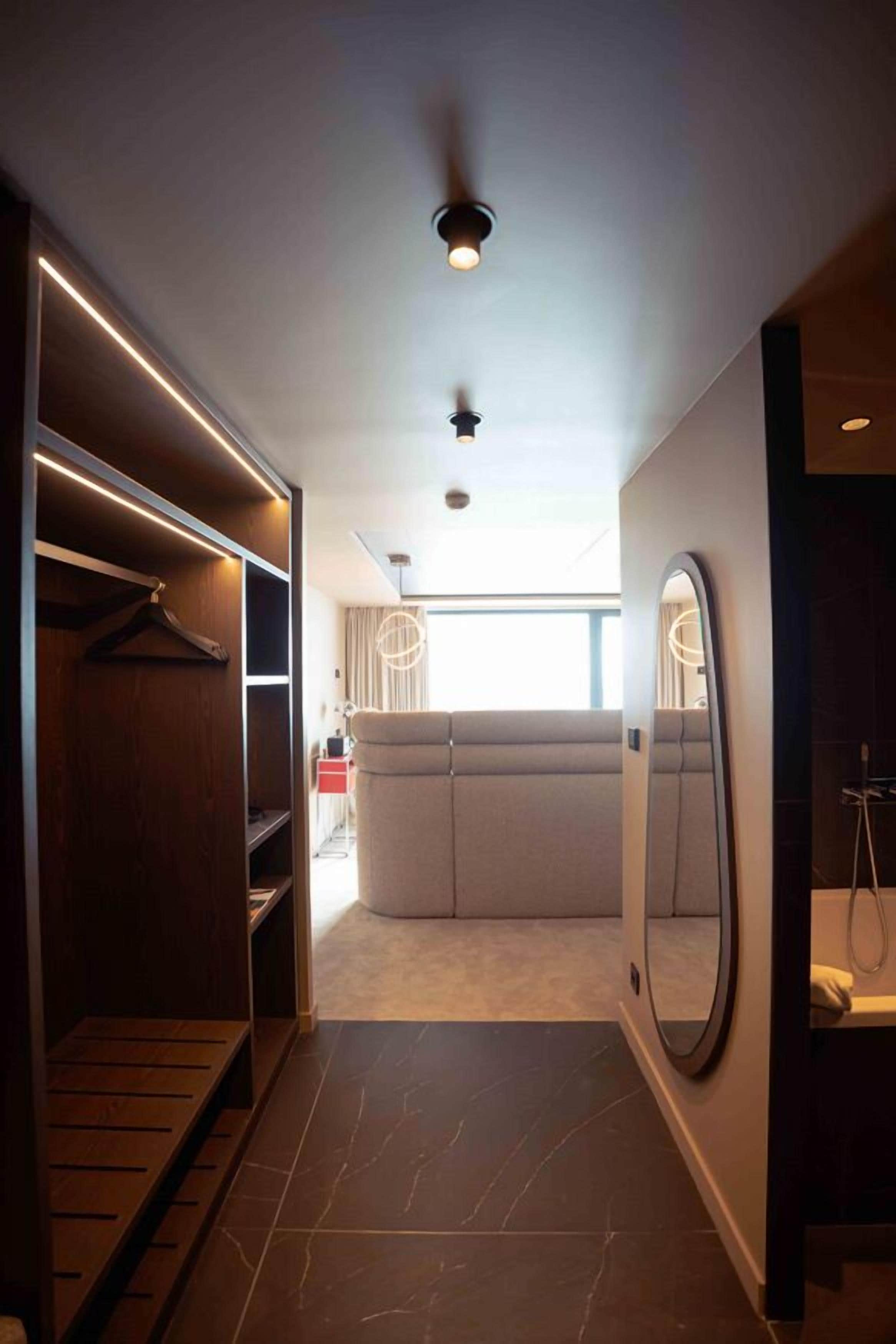 A modern hotel room with a walk-in closet, a large mirror, and a view of the city.