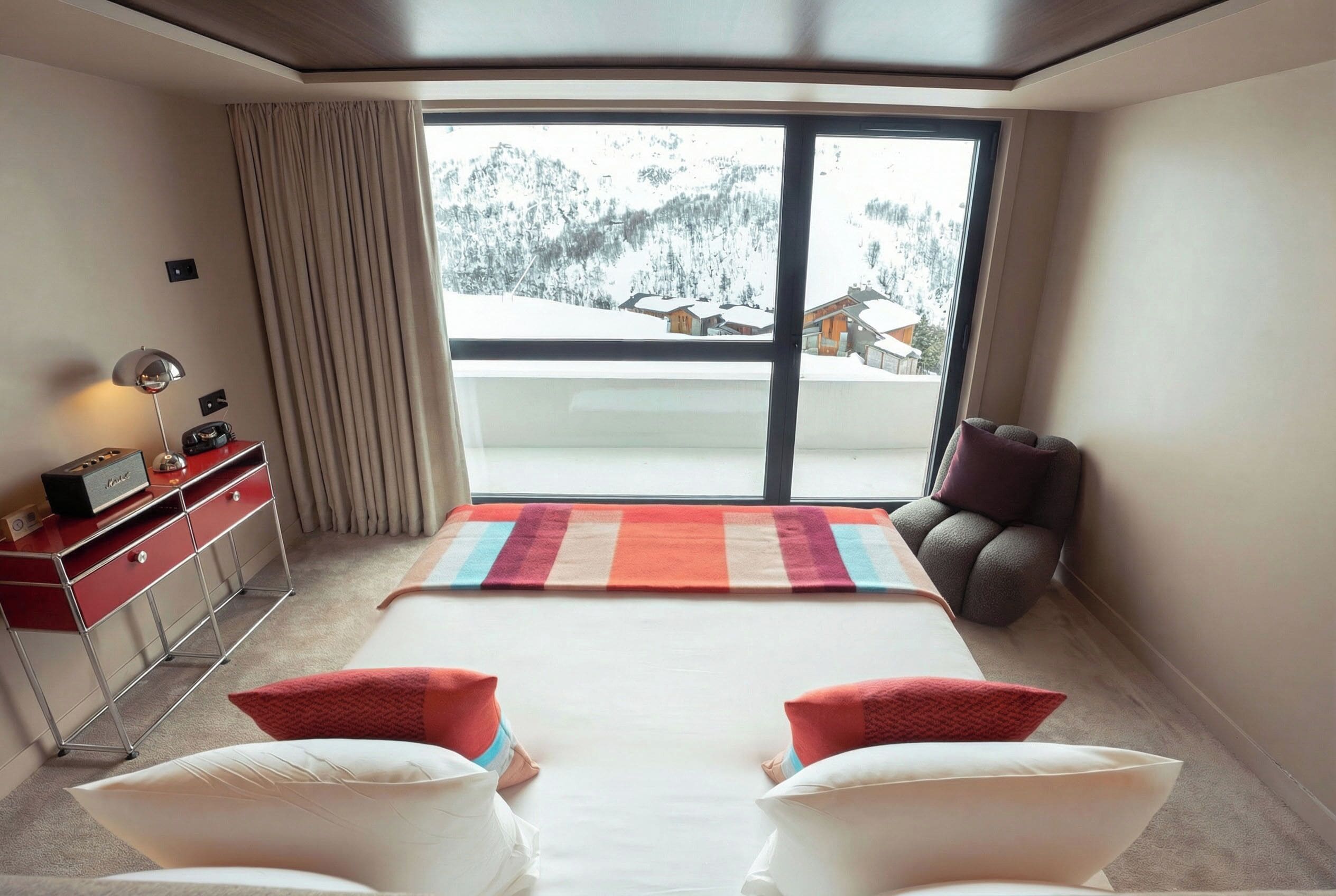 Una habitación de hotel con una cama, un escritorio, una silla, una ventana que ofrece vistas de montañas nevadas y una cortina.