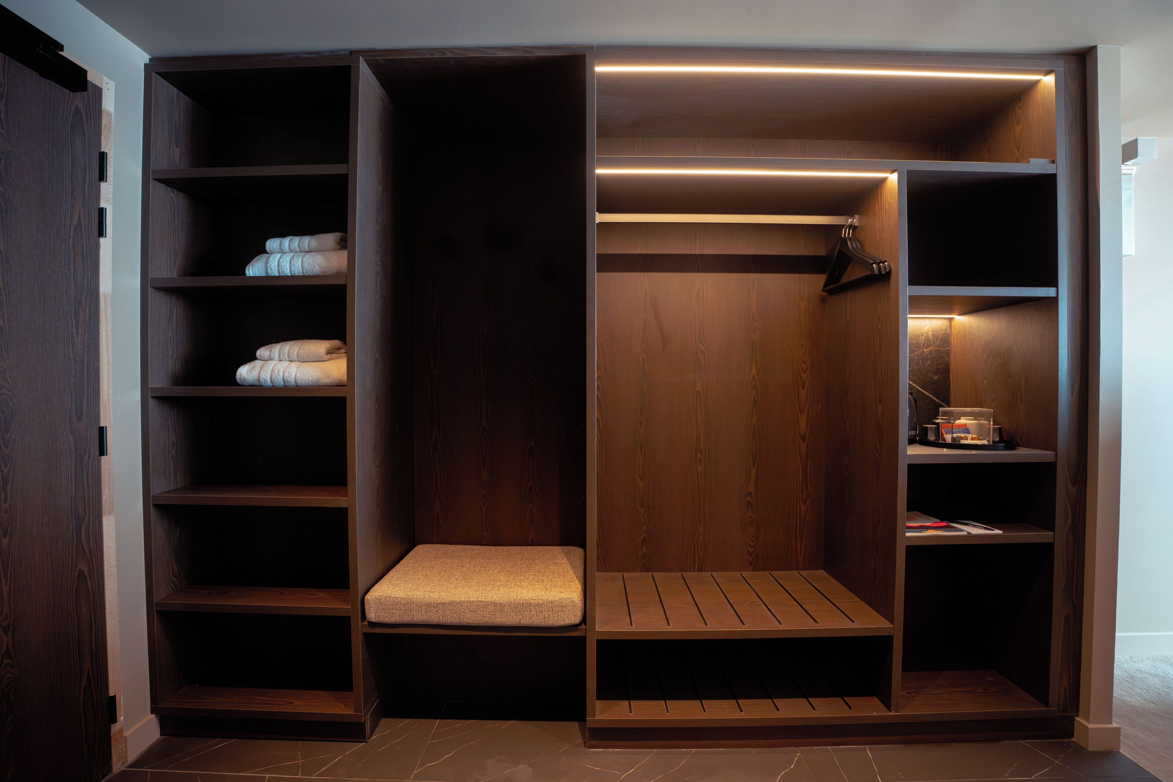 A walk-in closet with multiple shelves, a bench, and a hanging rod.