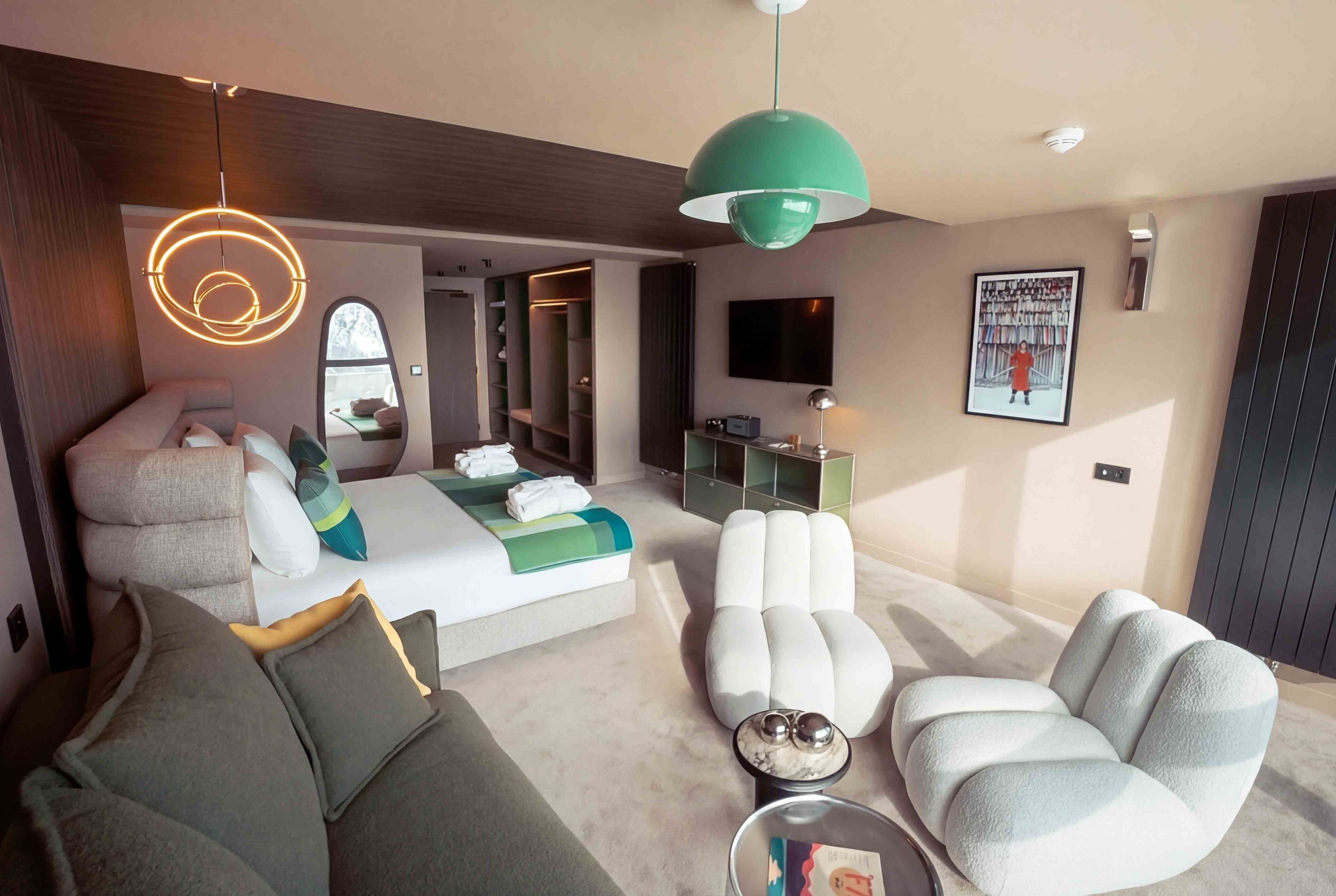 Une chambre d’hôtel moderne avec un canapé, un fauteuil et un lit agrémenté d’une touche de vert.