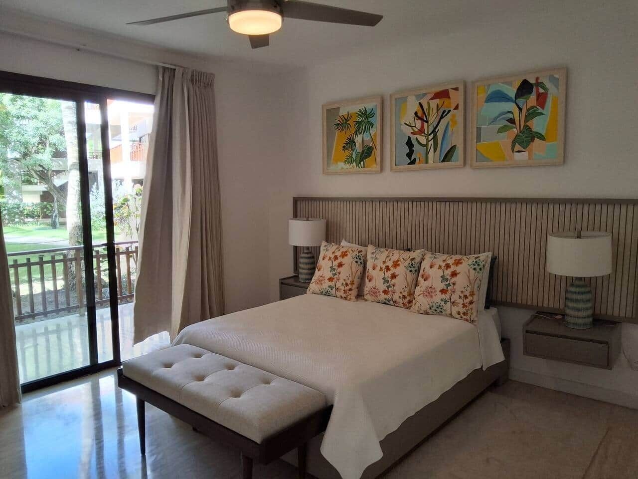 Ein Schlafzimmer mit einem großen Bett, einem Deckenventilator, einer Schiebetür zu einem Balkon und drei gerahmten Kunstwerken an der Wand.