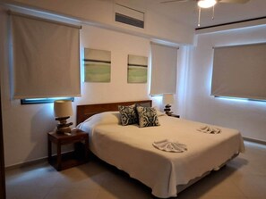 A neatly made bed with a white bedspread, two decorative pillows, a bedside lamp, and a small table with a lamp. - Amazing two bedroom Penthouse at Aligio Aparthotel (Las Terrenas)