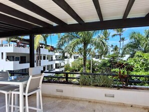 A covered outdoor seating area with a view of a multi-story building and palm trees. - Amazing two bedroom Penthouse at Aligio Aparthotel (Las Terrenas)