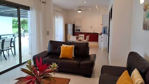 Ein modernes Wohnzimmer mit einer Couch, einem Couchtisch mit Pflanze und Blick auf eine Küche und einen Essbereich.