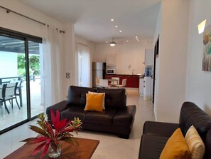 A modern living room with a sofa, a coffee table with a plant, and a view of a kitchen and dining area. - Amazing two bedroom Penthouse at Aligio Aparthotel (Las Terrenas)