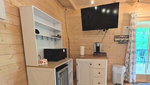 Een houten interieur met een aan de muur bevestigde televisie, een klein kastje, een magnetron en een prullenbak.