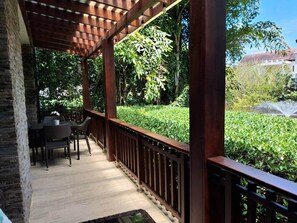Ein überdachter Außenbereich mit Holzterrasse, Tisch und Stühlen sowie Blick auf Garten und Gebäude im Hintergrund.