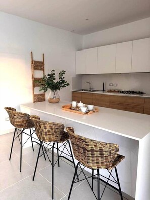 A modern kitchen with white cabinets, a central island with bar stools, and a decorative plant. - Stunning condo, private rooftop pool, best in LT (Las Terrenas)
