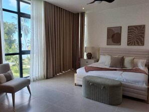 A bedroom with a bed, a chair, a nightstand, and a large window with curtains. - Stunning condo, private rooftop pool, best in LT (Las Terrenas)