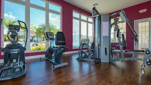 Ein Fitnessstudio mit Cardiogeräten, Gewichten und großen Fenstern mit Blick auf Palmen.