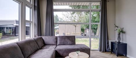 Una sala de estar moderna con un sofá modular, una mesa redonda de madera y vistas al exterior a través de amplias ventanas.