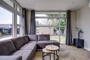 Ein modernes Wohnzimmer mit einer Eckcouch, einem runden Holztisch und Blick durch große Fenster ins Freie.