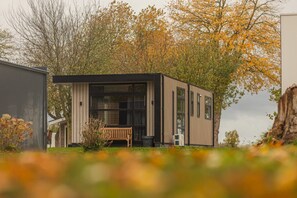 Een modern, laag gebouw met een groot raam, een bankje en een boom op de achtergrond.