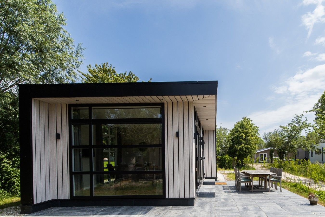 Un bâtiment moderne doté d’une grande baie vitrée, d’un espace extérieur aménagé pour s’asseoir et d’une terrasse dallée.