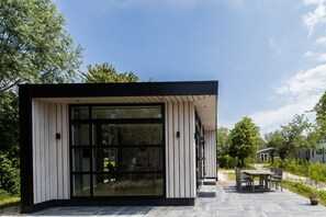 Un edificio moderno con un amplio ventanal, asientos exteriores y un patio empedrado.