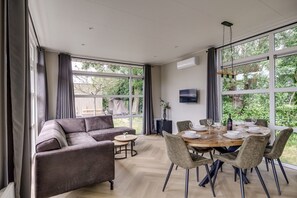 Uma sala de estar moderna com sofá, mesa de jantar, cadeiras e grandes janelas com vista para o exterior.