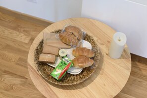 A round wooden table with a woven placemat, containing a plate with bread, a candle, and a juice box. - Room with Néron View in the Heart of Chartreuse (Quaix-en-Chartreuse)