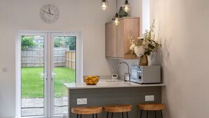 Eine moderne Küche mit integrierter Kochinsel, Barhocker, Pendelleuchten und Blick auf den Garten.
