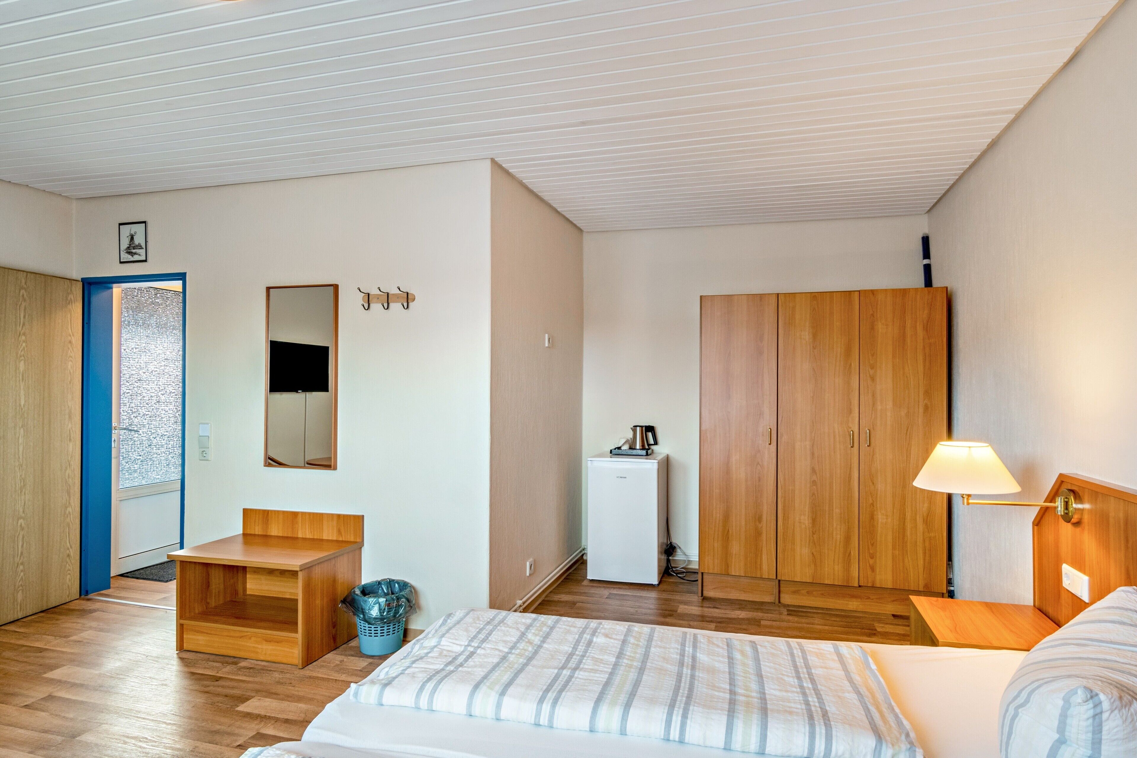 Quarto de hotel com cama, escrivaninha, guarda-roupa, pequena cozinha e banheiro.