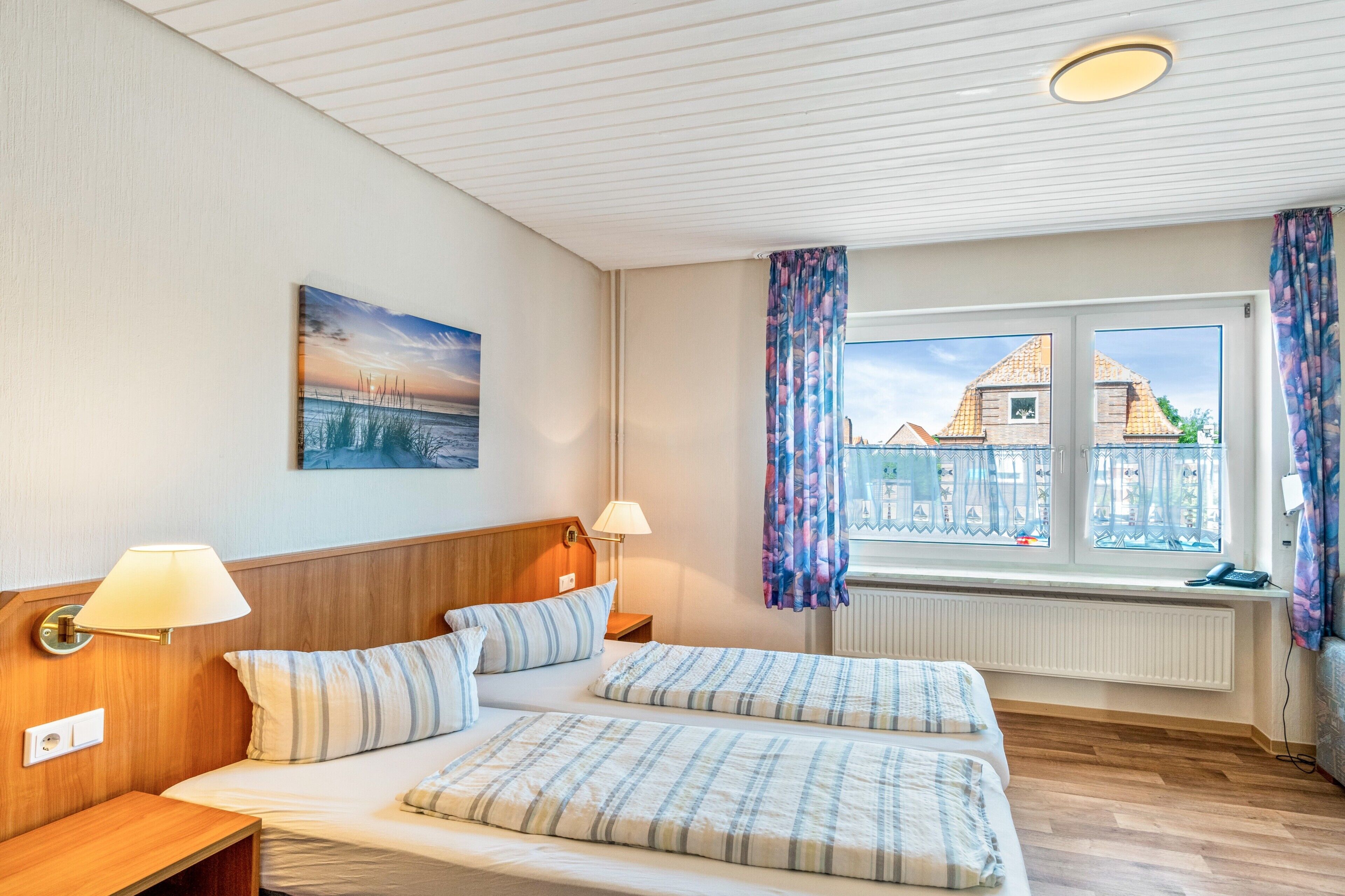 Ein Hotelzimmer mit einem Bett, zwei Nachttischlampen, einem Bild an der Wand und einem Vorhangfenster.