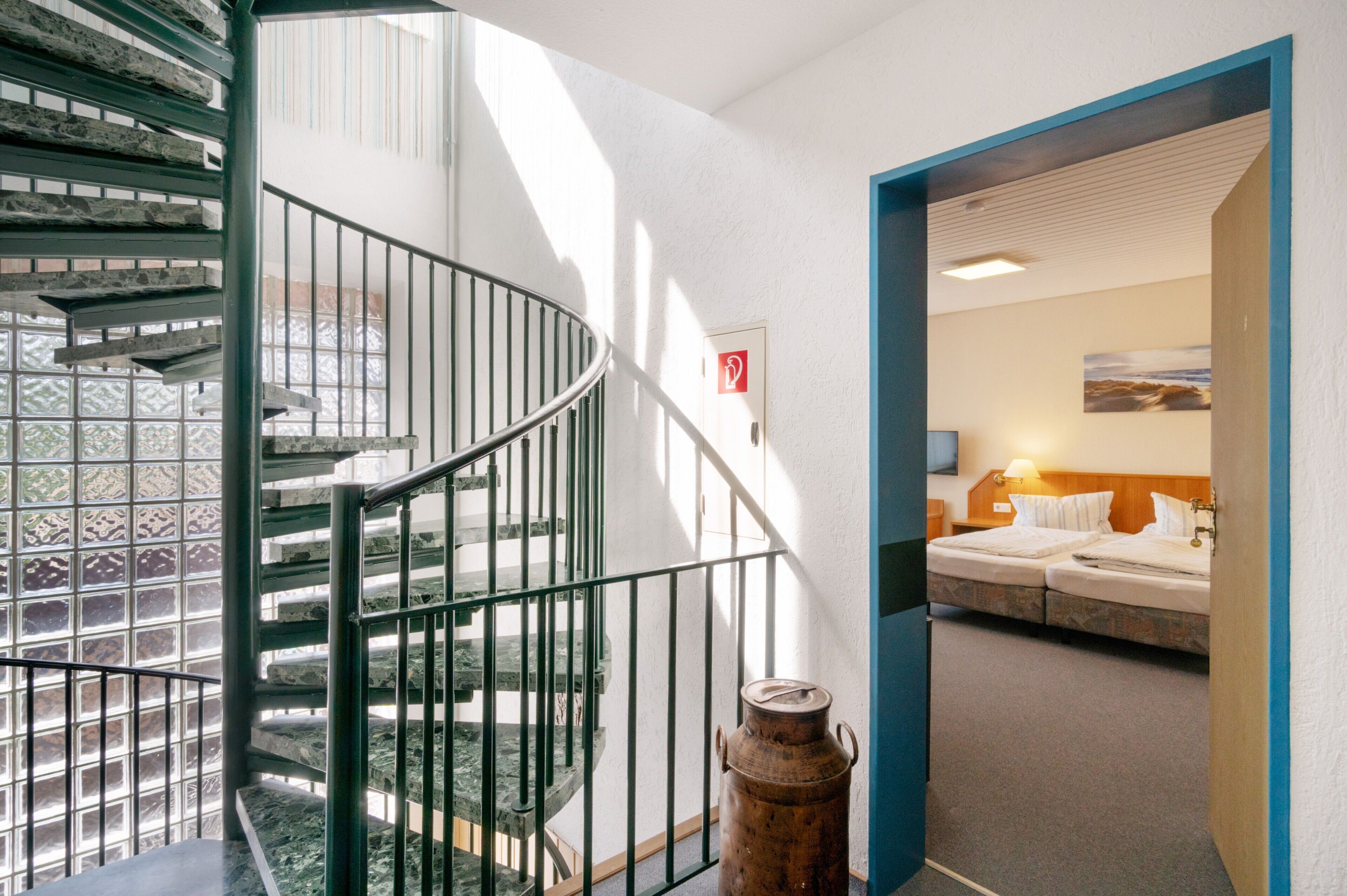 Eine Wendeltreppe mit Metallgeländern und Blick auf ein Schlafzimmer mit Bett und Nachttisch.