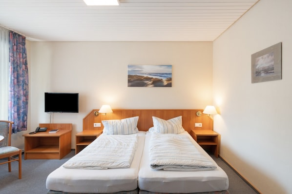 Habitación de hotel con dos camas, un televisor de pantalla plana, un escritorio con teléfono y una silla.