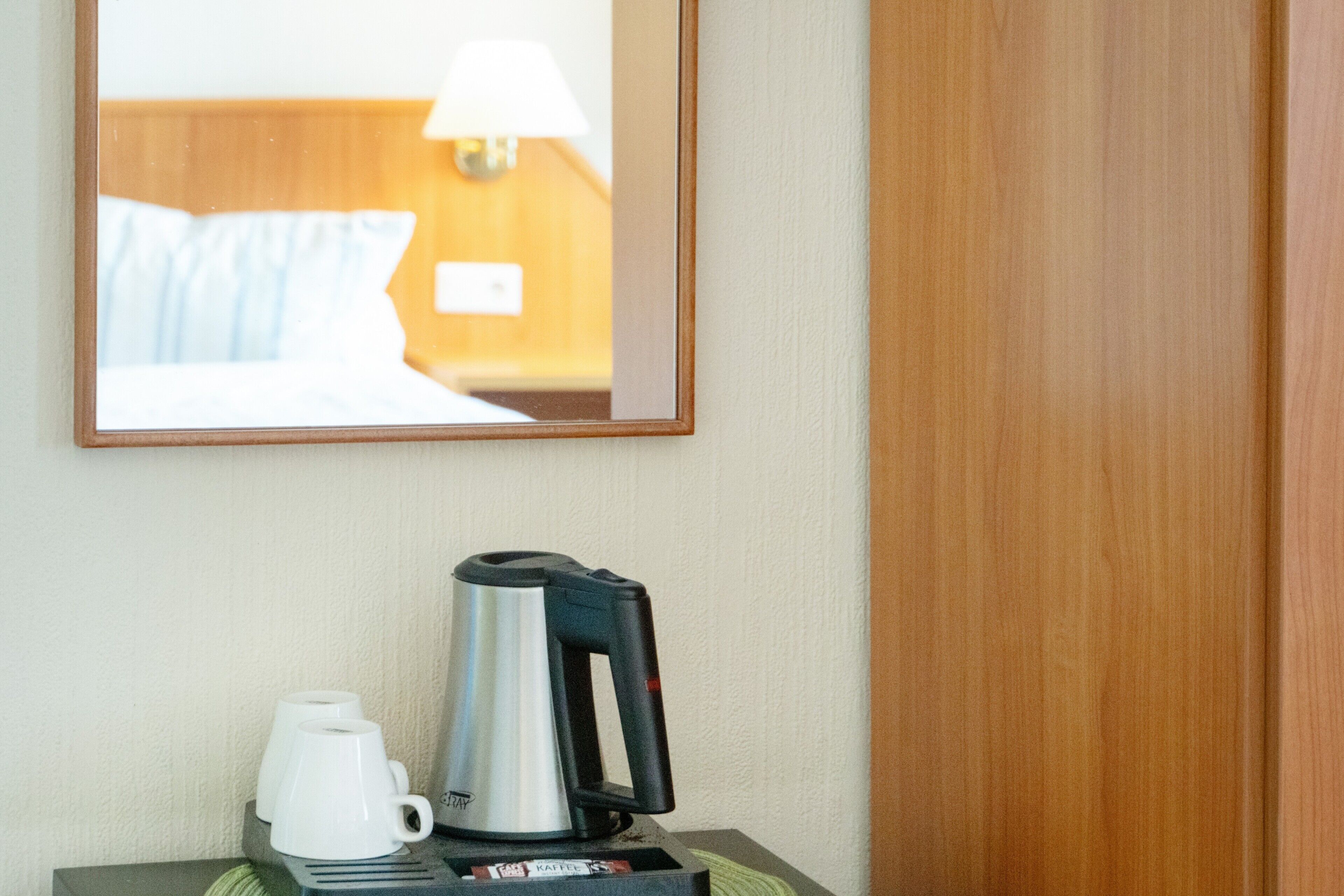 Een hotelkamer met een bed, een lamp, een koffiezetapparaat en een kopje op een tafel.