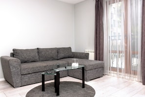 A modern living room with a grey sofa, a glass coffee table, and a round rug.