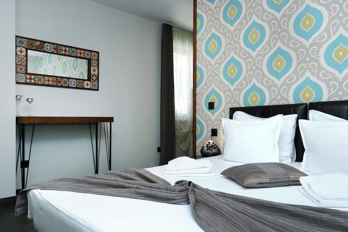 A neatly made bed with white linens, a bedside table with a lamp, and a patterned wall.