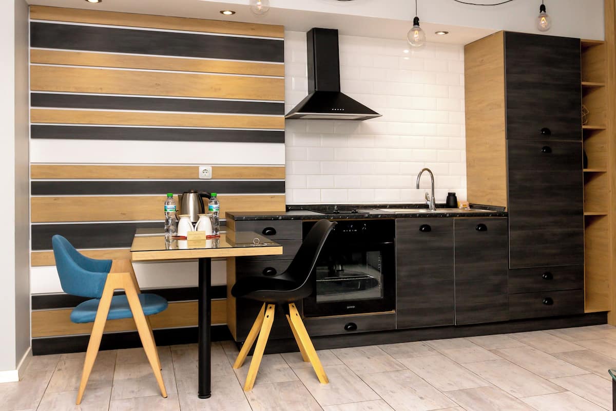 A modern kitchen with a wooden and black color scheme, a built-in oven, and a dining area with two chairs.