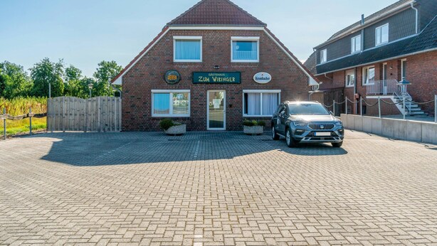 A two-story brick building with a sign reading 'Zum Wiking' and a parked car in front. - Room 'Doppelzimmer 2 Gästehaus' with Shared Terrace and Wi-Fi (Dornum)