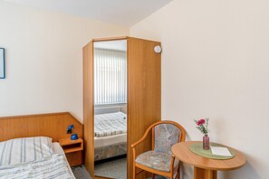 Hotellihuone, jossa on sänky, työpöytä lampun kanssa, tuoli, pieni pöytä maljakolla ja ikkuna, jossa on sälekaihtimet.