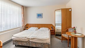 A hotel room with a double bed, a bedside table with a lamp, a chair, a small table with a vase, and a mirror. - Room 'Doppelzimmer 2 Gästehaus' with Shared Terrace and Wi-Fi (Dornum)