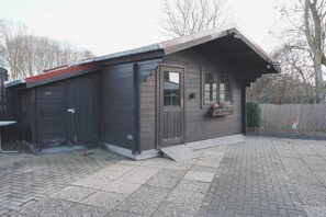 Ein kleines, dunkelbraunes Holzgebäude mit schrägem Dach, einer Tür und einem Fenster mit Blumenkasten.