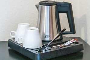 A stainless steel kettle, two white mugs, and a packet of tea on a black tray.