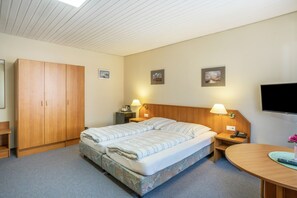 Una habitación de hotel con cama, armario, escritorio con lámpara, televisor y obras de arte en las paredes.