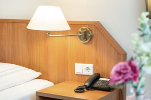 A hotel room with a wooden headboard, a bedside lamp, a telephone, and a power outlet.