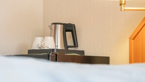 Une chambre d’hôtel avec un lit, une table de chevet équipée d’une bouilloire, de tasses et d’une lampe.