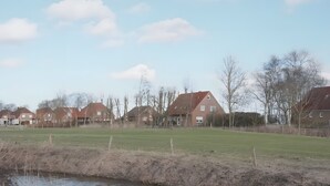 Un plan d’eau paisible, bordé d’une rive herbeuse et entouré de maisons aux toits rouges.