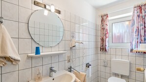 A bathroom with a sink, mirror, toilet, and a window with curtains. - Room 'Doppelzimmer 4 Gästehaus' with Shared Terrace and Wi-Fi (Dornum)