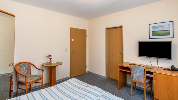 A hotel room with a bed, two chairs, a desk, a television, and a door. - Room 'Doppelzimmer 4 Gästehaus' with Shared Terrace and Wi-Fi (Dornum)