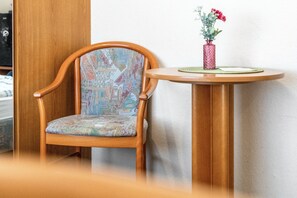 A wooden chair with a patterned cushion and a small round table with a vase of flowers. - Room 'Doppelzimmer 4 Gästehaus' with Shared Terrace and Wi-Fi (Dornum)