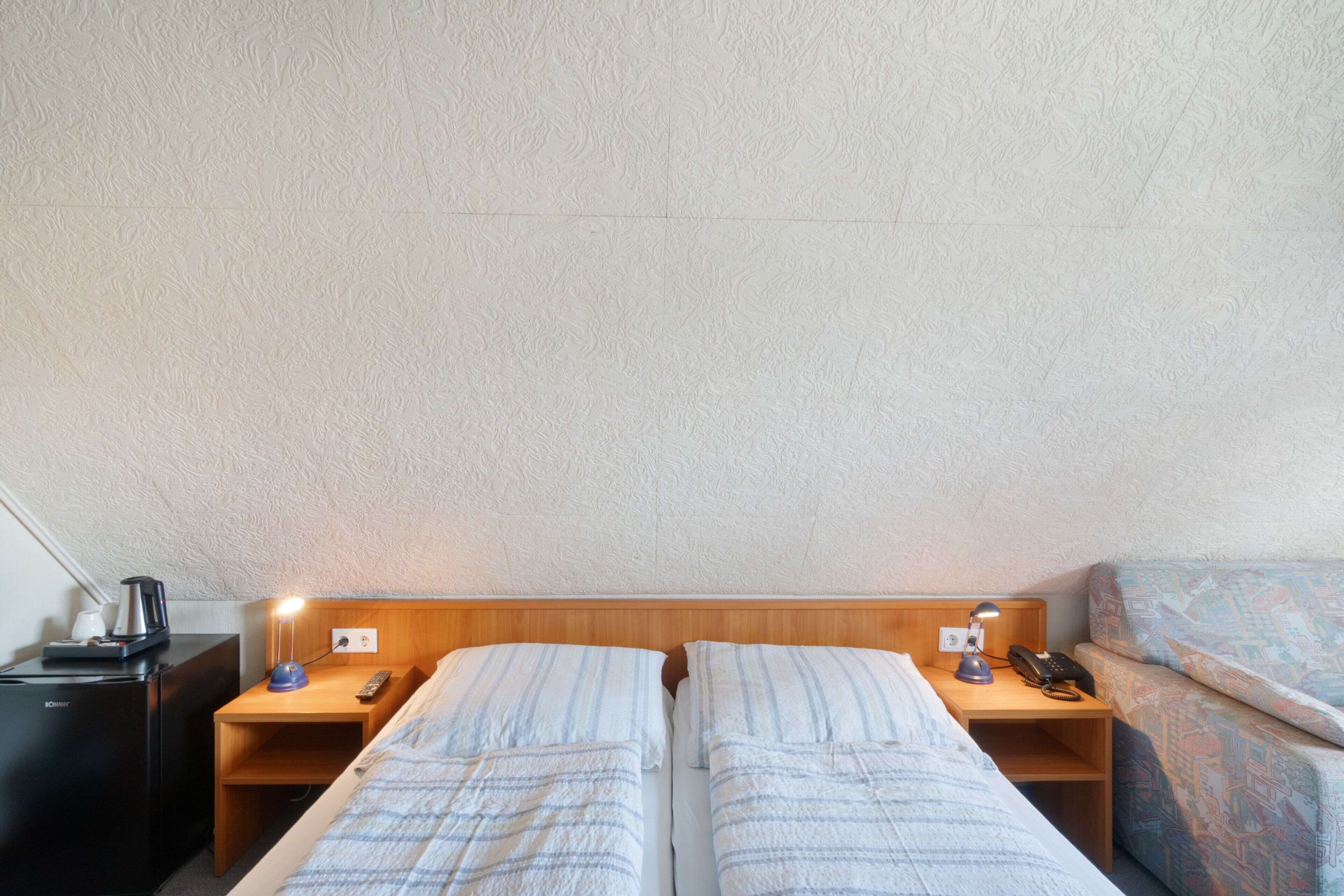 Een hotelkamer met twee bedden, een houten hoofdbord, nachtkastjes met lampen, een koffiezetapparaat en een telefoon.