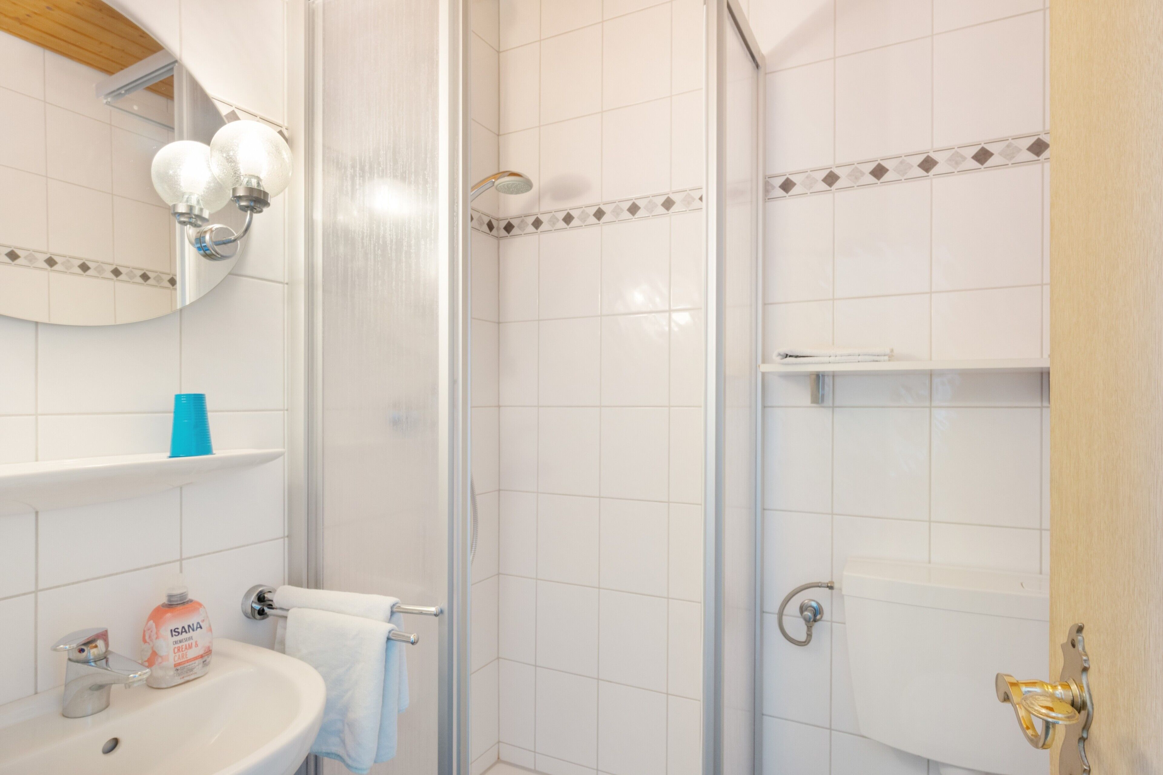 Ein Badezimmer mit weißem Waschbecken, einem Spiegel, einer Dusche und einem Handtuchhalter.